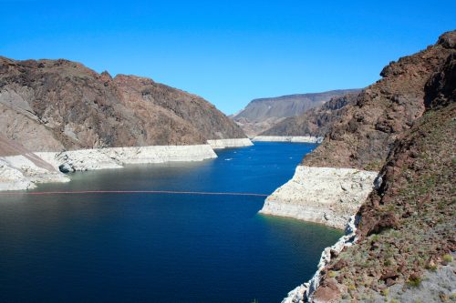 A serene lake surrounded by rocky cliffs under a clear blue sky, with a visible waterline and distant mountains.