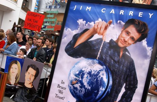 Crowd at a movie premiere holding signs, with a large poster of Jim Carrey holding a globe in the foreground.