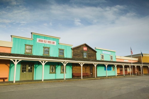 Colorful wooden storefronts line a western-style street under a cloudy sky.