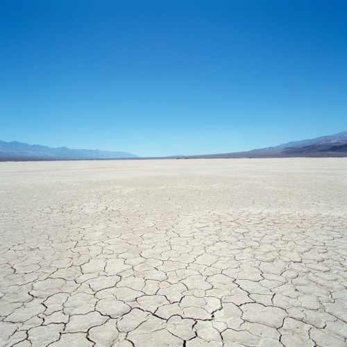 A vast, dry landscape with cracked earth under a clear blue sky and distant mountains on the horizon.