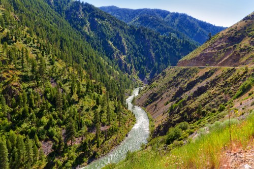 A winding river flows through a lush green valley surrounded by mountains and trees under a clear blue sky.