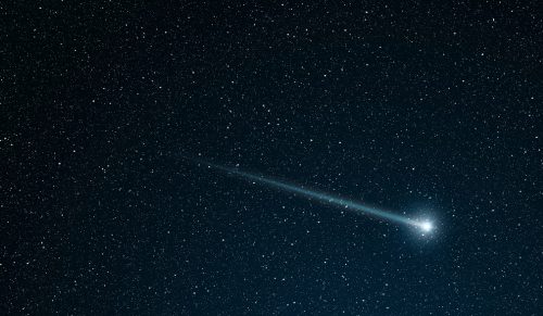 A bright comet streaks across a star-filled night sky, leaving a glowing trail behind it.