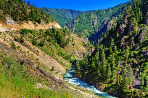 A scenic view of a river winding through lush green mountains under a clear blue sky.