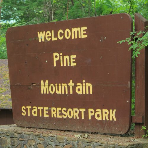 Wooden sign reading "Welcome Pine Mountain State Resort Park" surrounded by greenery.
