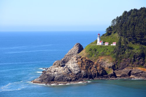 A scenic view of a lighthouse on a rocky coastline, surrounded by lush greenery and blue ocean waters.