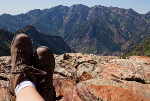 A pair of hiking boots resting on a rocky ledge, with a panoramic view of mountains in the background.