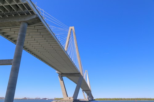 A modern cable-stayed bridge spans over a calm body of water under a clear blue sky.