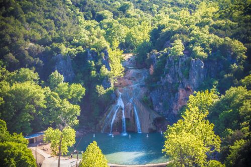 A scenic view of a waterfall cascading into a serene pool, surrounded by lush green trees and rocky cliffs.