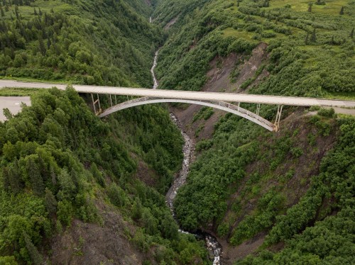 Aerial view of a curved bridge spanning a deep, green valley with a winding river below.