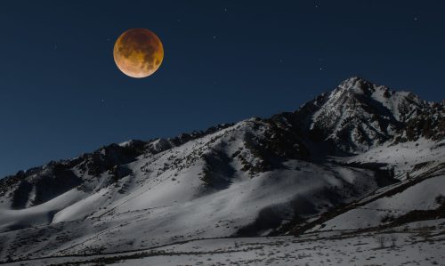 A snowy mountain landscape under a night sky, featuring a large, glowing moon. Stars are visible in the background.