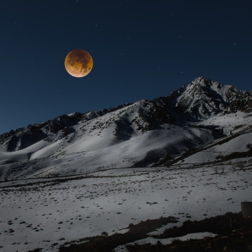 A snowy mountain landscape under a night sky, featuring a large, glowing moon. Stars are visible in the background.