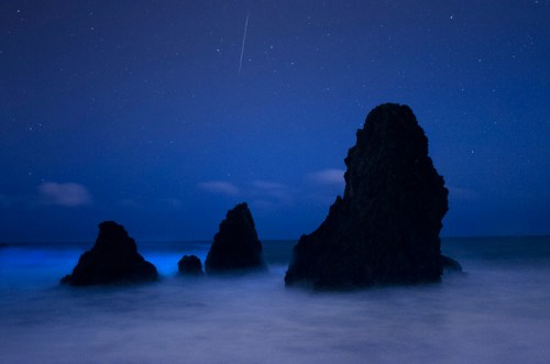 Silhouetted rock formations emerge from a misty ocean under a starry night sky.