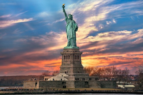 The Statue of Liberty stands tall against a colorful sunset sky, symbolizing freedom and hope.