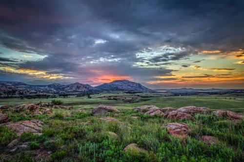 A scenic landscape featuring rolling hills, rocky outcrops, and a vibrant sunset sky with clouds.