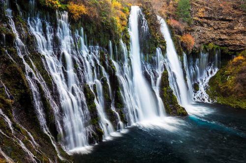 A scenic waterfall cascading over rocky cliffs into a serene pool, surrounded by autumn foliage.
