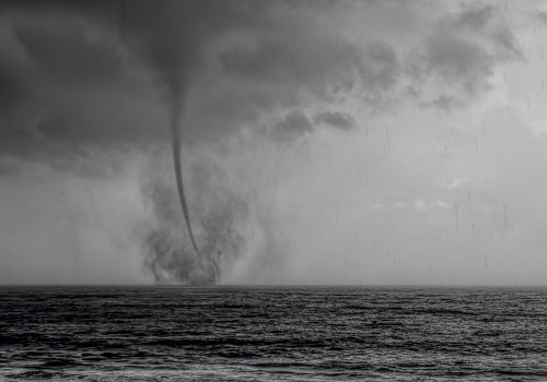 A dark waterspout forms over the ocean under a cloudy sky, with rain falling in the background.