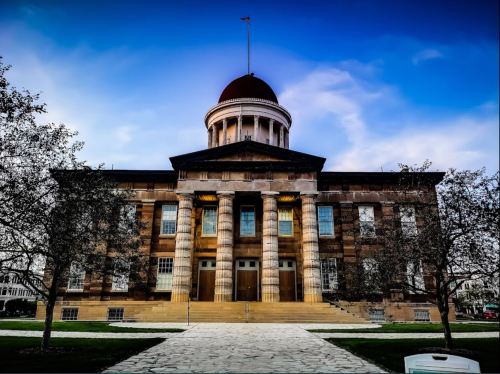 Historic building with a dome and columns, surrounded by trees under a blue sky.