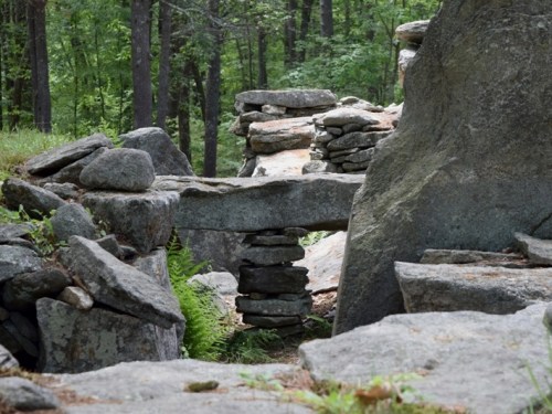 A stone bridge made of stacked rocks connects two larger boulders in a forested area.