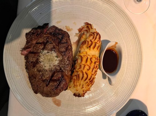 A plate featuring a grilled steak with a side of creamy potato and a small dish of sauce.