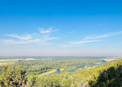 A panoramic view of a river winding through lush green fields under a clear blue sky.