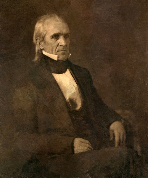 Portrait of a middle-aged man in formal attire, seated with a serious expression against a dark background.