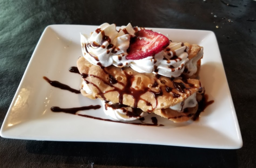 A plate of waffles topped with whipped cream, chocolate drizzle, and a slice of strawberry.