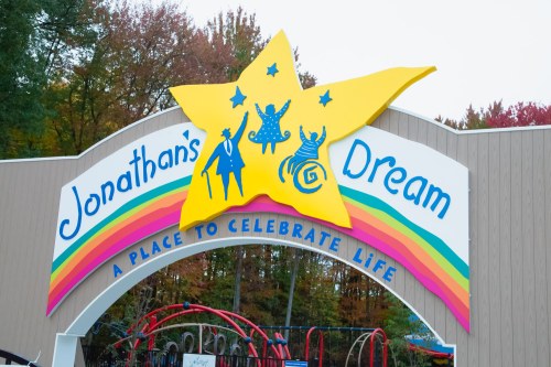 Colorful entrance sign for "Jonathan's Dream," featuring a large star and playful figures, set against a backdrop of trees.