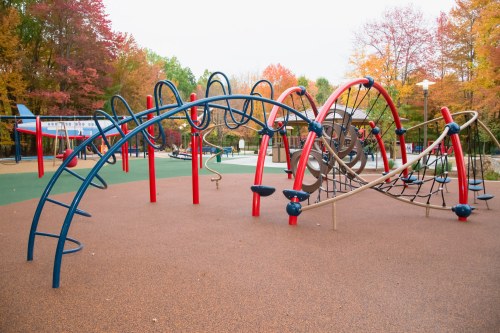 Colorful playground equipment with climbing structures, surrounded by autumn trees with vibrant foliage.