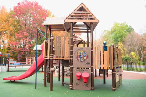 Colorful playground structure with a slide, climbing features, and musical elements, surrounded by autumn foliage.