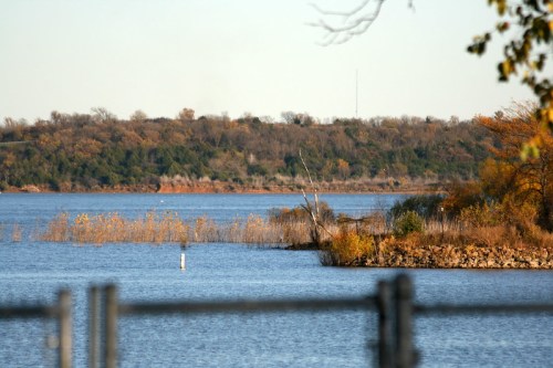 A serene lake surrounded by autumn foliage and distant hills under a clear sky.