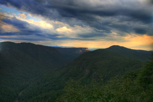 A panoramic view of lush green mountains under a dramatic sky with clouds and a hint of sunset light.