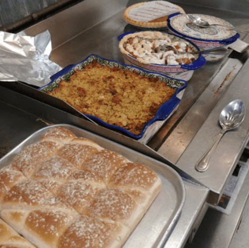 A variety of dishes including baked casserole and rolls on a countertop, with serving utensils nearby.