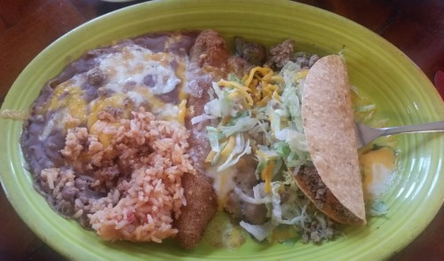 A vibrant plate featuring rice, refried beans, a taco with lettuce and cheese, and a side of crispy fried food.