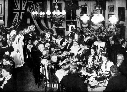A large gathering in a decorated dining room, with guests in formal attire enjoying a festive meal.
