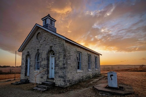 A historic stone building at sunset, featuring a bell tower and surrounded by open fields.