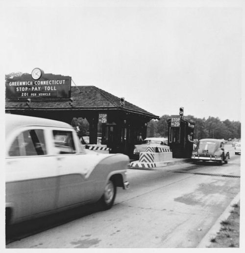 Black and white photo of a toll booth in Greenwich, Connecticut, with cars approaching and a sign displaying toll rates.