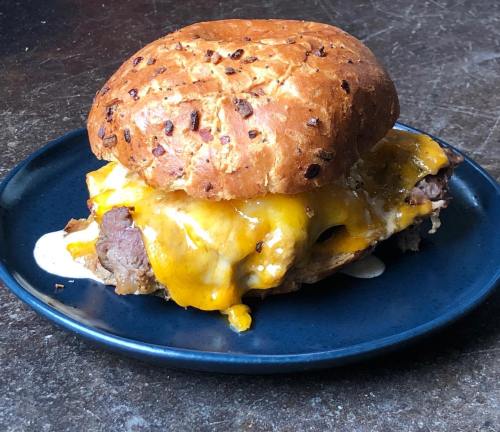 A hearty sandwich with melted cheddar cheese, beef, and a toasted onion roll on a dark plate.