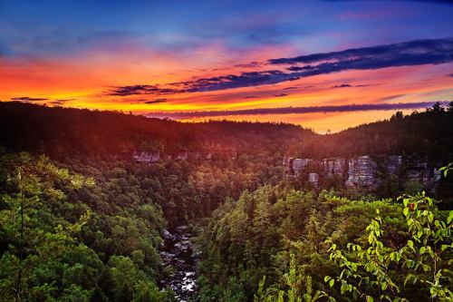 A vibrant sunset over a lush green valley, with cliffs and a winding river below, creating a serene natural landscape.