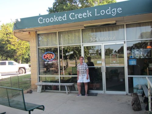 A woman stands outside Crooked Creek Lodge, featuring an "Open" sign and a welcoming entrance.