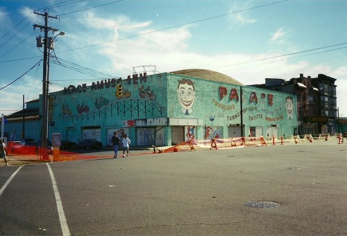 A colorful mural on a large building, featuring playful designs and characters, with construction barriers in the foreground.