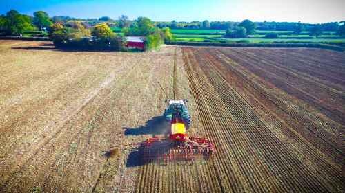 Aerial view of a tractor plowing a large, empty field under a clear blue sky.