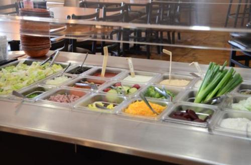 A salad bar with various toppings including lettuce, tomatoes, cheese, and vegetables in clear containers.