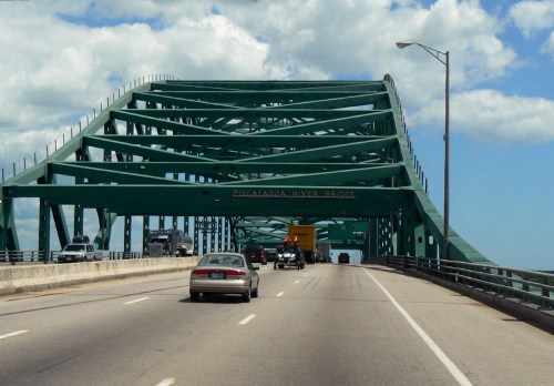 View of the Piscataqua River Bridge with vehicles traveling on the roadway under a blue sky with clouds.