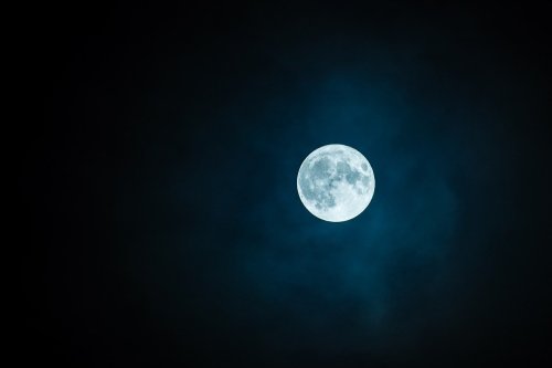 A bright full moon glowing in a dark, cloudy night sky.