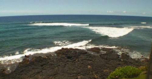 A serene ocean view with gentle waves breaking on rocky shore under a clear blue sky.