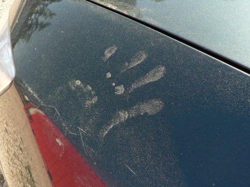A dusty car surface with a handprint and several finger marks visible on the dark paint.