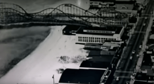 Aerial view of a beachside amusement park with a roller coaster and nearby buildings along a sandy shore.