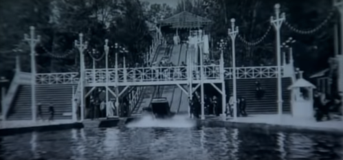 A vintage black-and-white photo of a water ride with people on a platform and a boat splashing into the water.