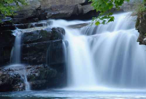 A serene waterfall cascading over rocky ledges, surrounded by lush greenery and smooth water.