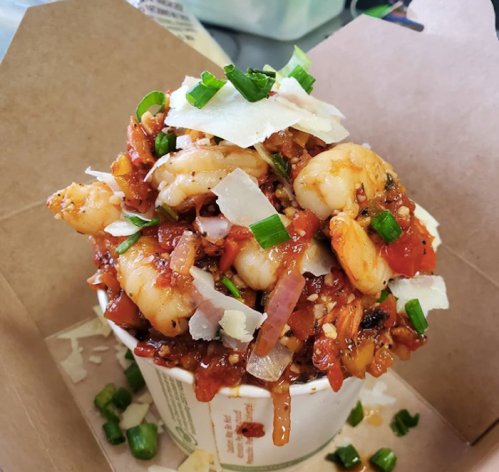 A cup filled with shrimp, diced vegetables, herbs, and cheese, topped with green onions.